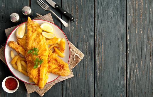 Two pieces of battered fish on a plate with chips on a wooden table with space