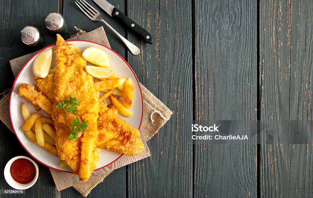 Fish and chips background Two pieces of battered fish on a plate with chips on a wooden table with space Fish Stock Photo