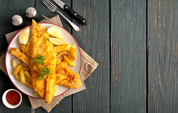 Fish and chips background Two pieces of battered fish on a plate with chips on a wooden table with space fried photos stock pictures, royalty-free photos & images