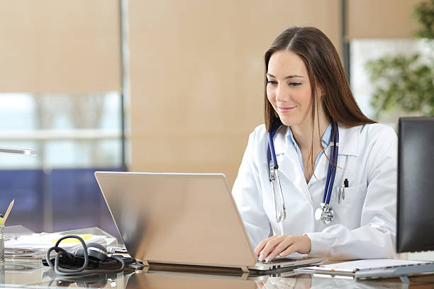 Doctor working on line in a consultation Concentrated doctor working on line with a laptop sitting in a desk in a consultation entering data stock pictures, royalty-free photos & images