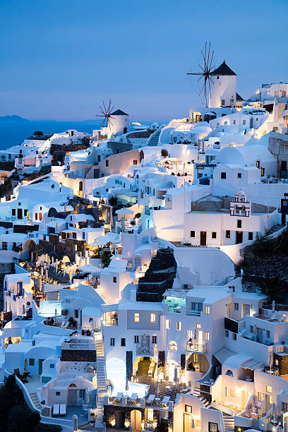 Santorini's city Oia illuminated at dusk, Santorini Island, Greece. Windmills are seen in the background. Long exposure with tripod, 50 megapixel image.