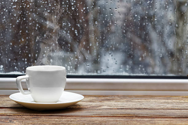 White cup on wooden windowsill White steaming cup of hot tea or coffee on vintage wooden windowsill or table against window with raindrops on blurred background. Shallow focus. rainy cafe stock pictures, royalty-free photos & images