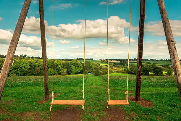 Handmade swings of wood and ropes in the middle of a field a glorious sunny day. Ideal scenic image.