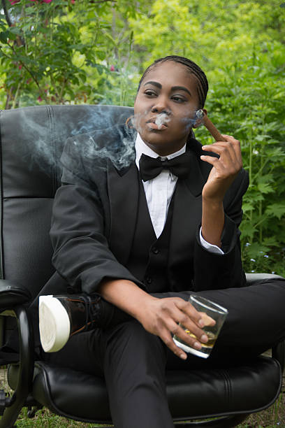 giovane donna di colore in resistenza maschile, grave, che fuma un sigaro. - smoking women smoke smoking issues foto e immagini stock