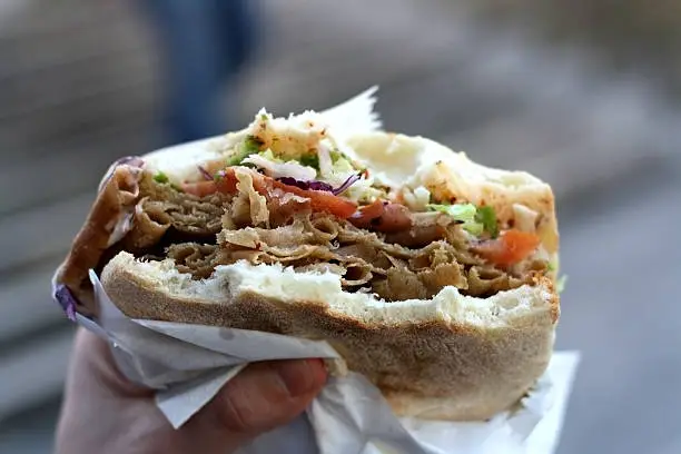 Doner kebab stuffed into a pita with tomatoes, cabbage and lettuce. Eating outdoor. Selective focus.