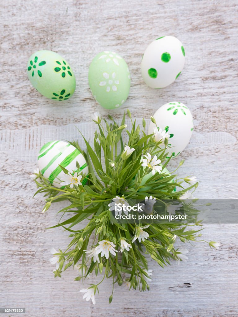Easter eggs and white wild flowers composition White and green easter eggs decorated by stripes, dots and flowers and wild flowers bouquet on the white wooden board Affectionate Stock Photo