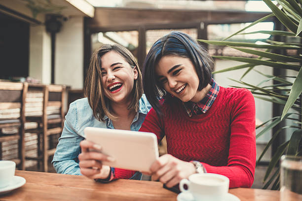 dos frineds femeninos sosteniendo la tableta y riendo en la cafetería - telecommunications equipment discussion telephone horizontal fotografías e imágenes de stock
