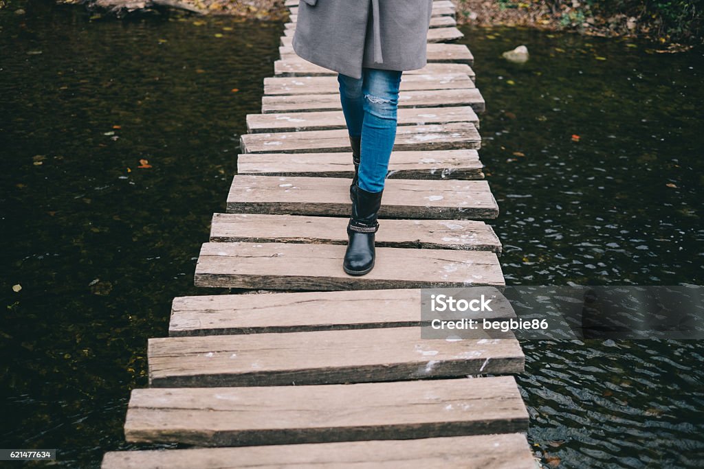 Young woman crossing a wooden bridge Young woman crossing a wooden bridgeYoung woman crossing a wooden bridge Adult Stock Photo