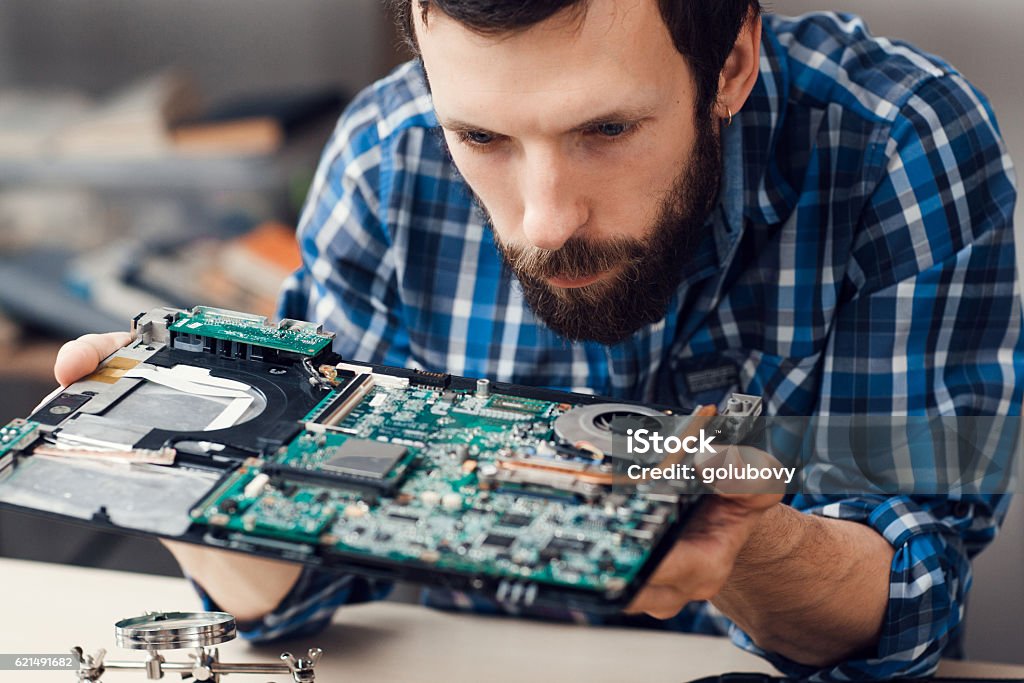 Engineer studying computer motherboard, close-up Engineer studying computer motherboard, close-up. Bearded repairman examing electronic circuit to find failure issue. Repair shop, technology, occupation concept Computer Stock Photo