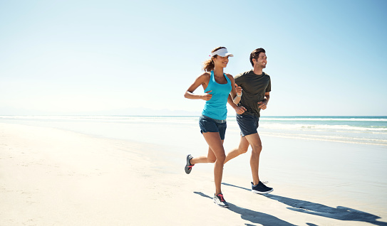 Shot of a young couple running along the beach together