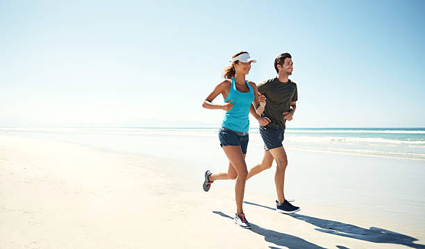 Working out by the ocean Shot of a young couple running along the beach together surge stock pictures, royalty-free photos & images