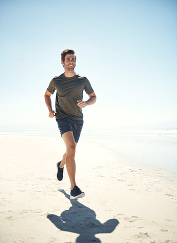 Shot of a sporty young man running along the beach
