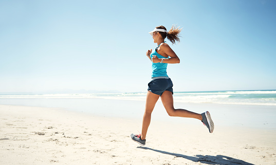 Shot of a sporty young woman running along the beach