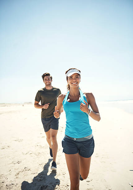 Everything's better at the beach Shot of a young couple running along the beach together healthy lifestyle women outdoors athlete stock pictures, royalty-free photos & images
