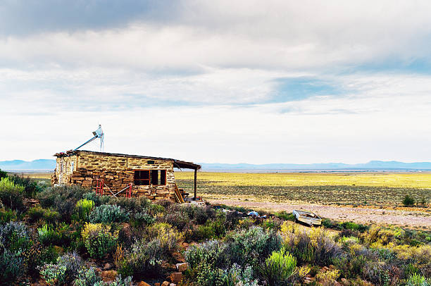 A tiny cottage built of stone on a remote farm in South Africa's semi-desert Karoo region and surrounded by fields and the low, indigenous vegetation known as fynbos. Copy space on the clouded sky.