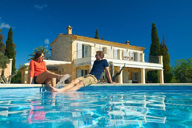 view from swimming pool at couple sitting in front of finca house on sunny day with clear blue sky