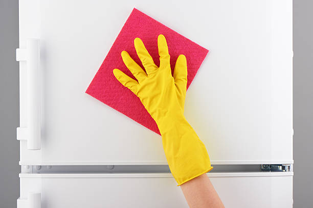 istock Hand in yellow glove cleaning white refrigerator with pink rag 621498602