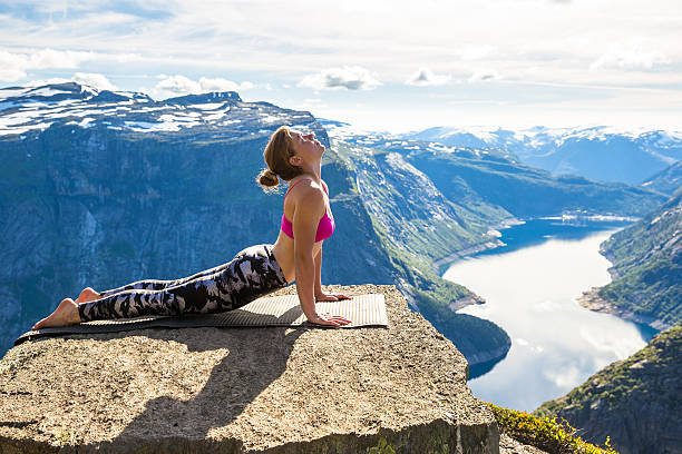 Young woman doing yoga on Trolltunga. Happy girl enjoy beautiful stock photo