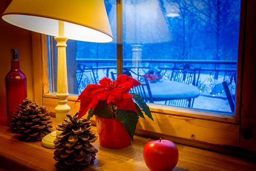 Warm lamp and xmas decorations on a windowsill, with winter landscape seen through the window.