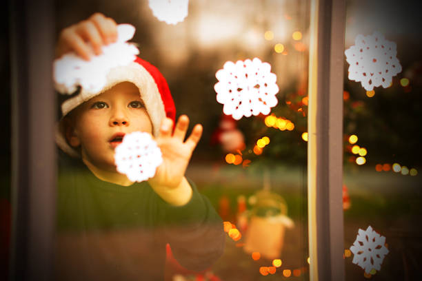 Kind schmückt ein Fenster mit Schneeflocken zu Weihnachten – Foto