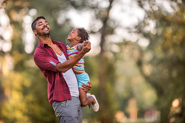 Happy African American father dancing with his cute daughter outdoors. Young happy father enjoying with his small girl in the park while dancing together. dancing dad stock pictures, royalty-free photos & images