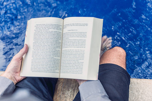 istock Adult man reading a book beside swimming pool 621571052