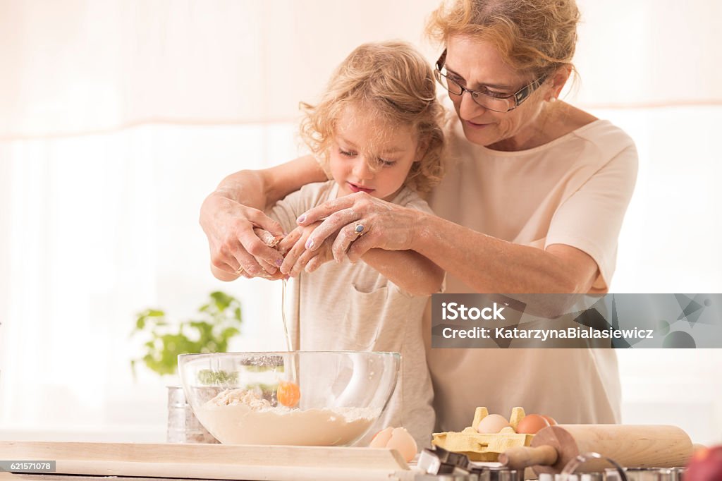 Child breaking the egg into a bowl Senior nanny helping child to break the egg into a bowl Grandmother Stock Photo