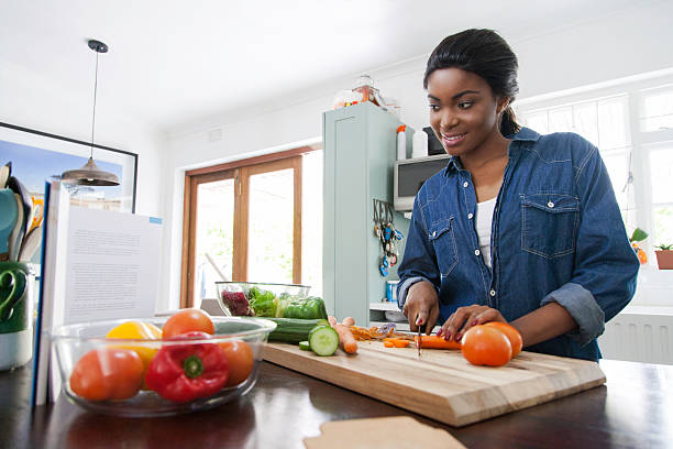 istock African female peeping the cookbook while chopping carrots. 621572494
