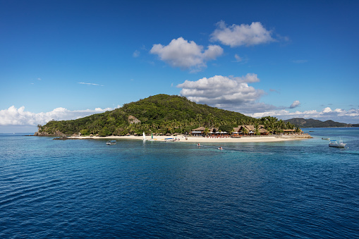 Lonely Castaway Island, also known as Qalito, located in the Mamanuca group of islands, surrounded by crystal clear water under blue summer sky. Fiji, Melanesia, Oceania.