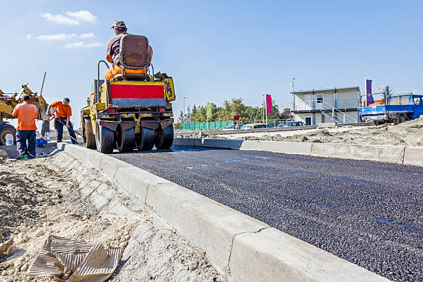 Hot asphalt is spreading with steamroller during road works Zrenjanin, Vojvodina, Serbia - September 23, 2015: Building activities during construction of the large complex shopping mall "AVIV PARK" in Zrenjanin city.  kerbstone stock pictures, royalty-free photos & images