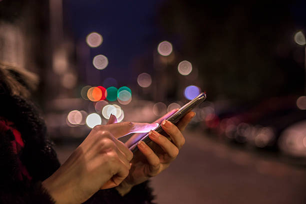 Woman using her mobile phone, city skyline night light backgroun Woman using her mobile phone, city skyline night light background mobile phone lights up stock pictures, royalty-free photos & images