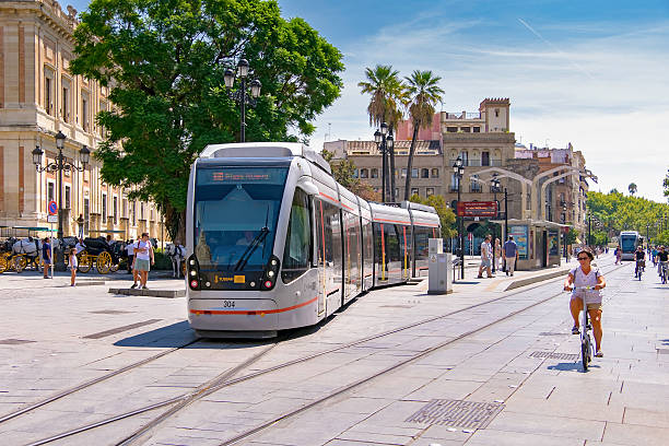 Seville, Spain - September 9, 2015: Seville trams blend with the historic city centre and co-exist with tourists, horse-drawn carriages, cyclists and pedestrians along car-free Avenida de la Constitución.   Key to this visual integration was the removal in 2011 of unsightly overhead wires replacing them with trams equipped with ACR (Acumulador de Carga Rápida) fast charging batteries allowing brief operation without an external electrical supply. 
