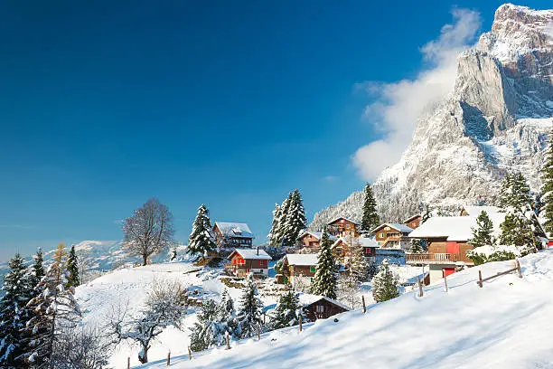 Travel to Switzerland in the winter. Alpine Village in the snow. Traditional houses with red shutters and roofs.