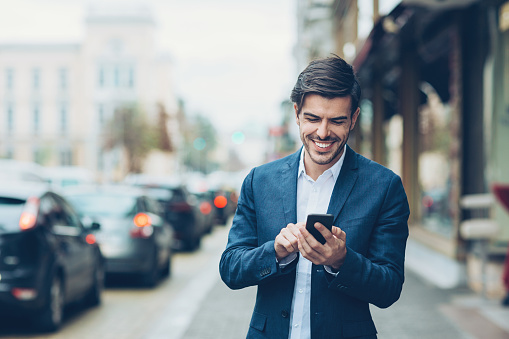Smiling businessman with smart phone outdoors on the street, with copy space.