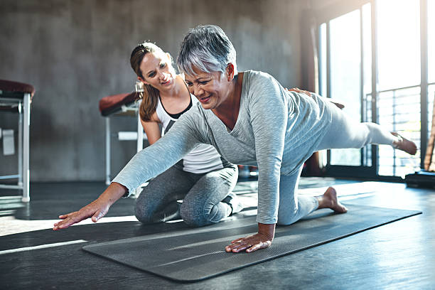 working together to improve muscle strength and tone - instructor exercising gym women imagens e fotografias de stock