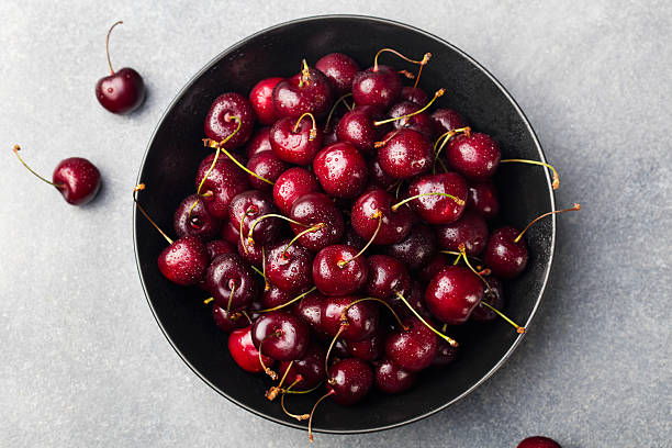 Fresh ripe black cherries in a black bowl on a grey stone background Top view.