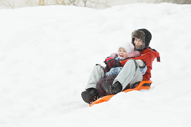 istock Siblings having downhill fun on winter orange plastic snow slider 621583518