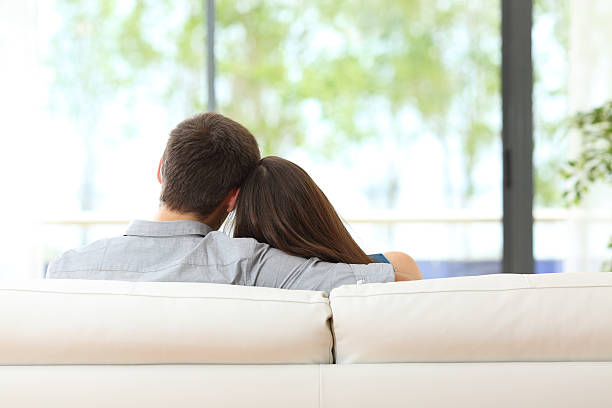 istock Couple sitting on a couch looking through window 621586682
