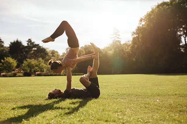Strong young couple doing acroyoga workout. Man and woman in park practising pair yoga in morning.