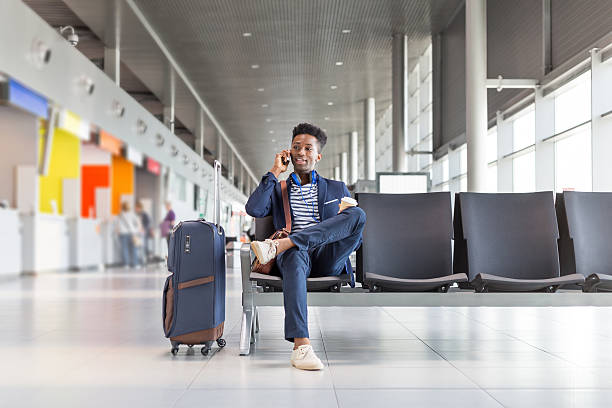 joven hablando por teléfono en la sala de espera del aeropuerto - airplane passenger indoors inside of fotografías e imágenes de stock