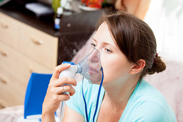 istock Young woman doing inhalation with a nebulizer at home 621596022