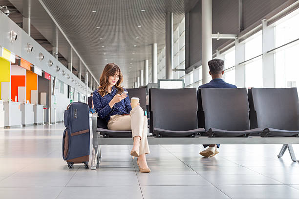 Woman waiting for flight at the airport lounge Young woman waiting for flight at the airport lounge. Businesswoman sitting on a bench with coffee and using a mobile phone. airports stock pictures, royalty-free photos & images
