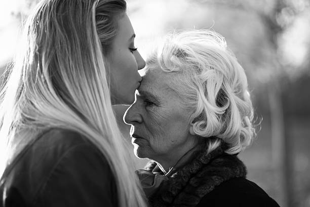 Grandmother and granddaughter in a park. Kiss! Cute girl kissing her granny. Profile. Black and white. forehead photos stock pictures, royalty-free photos & images
