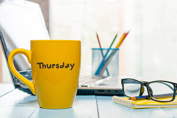 Thursday word written on yellow cup of coffee at maorning Thursday word written on yellow cup of coffee at maorning office workplace with laptop and glasses. wednesday morning stock pictures, royalty-free photos & images