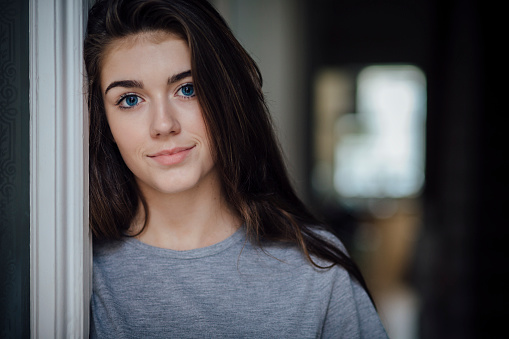 Portrait of a beautiful teenage girl. She has her head resting against the door frame.