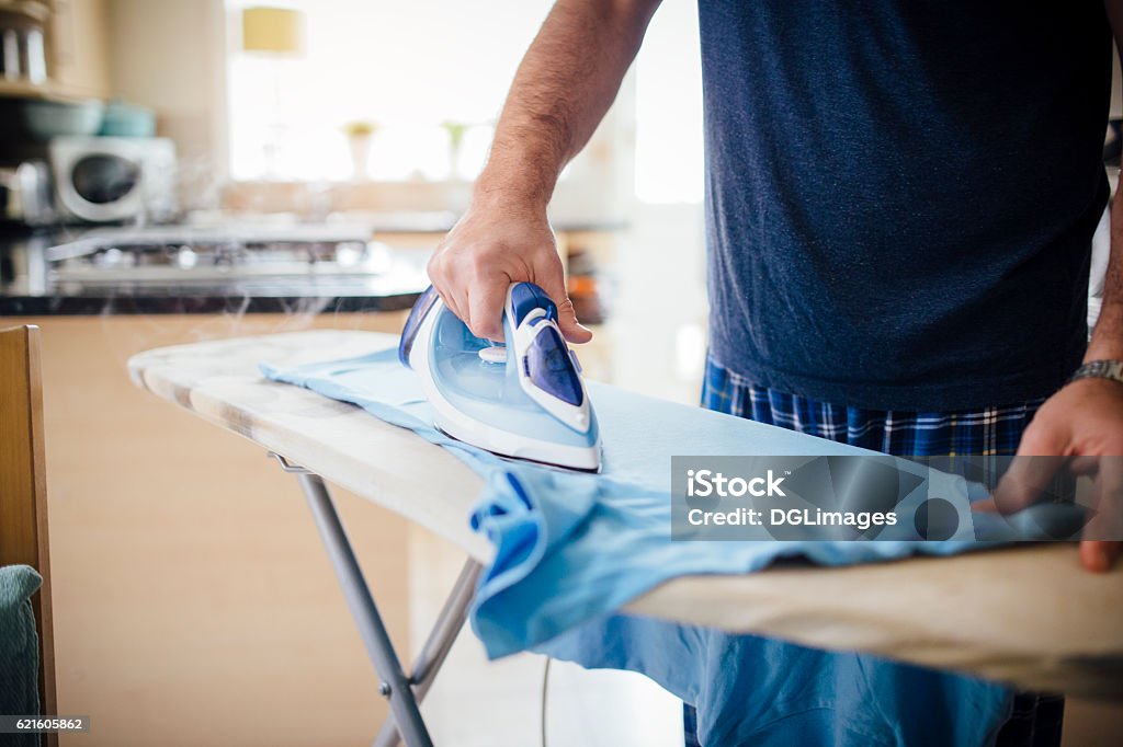 Man Ironing Laundry Close up of a mature man ironing a t-shirt in the kitchen. Iron - Appliance Stock Photo