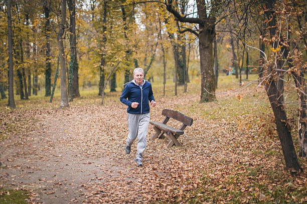 The photo of a senior man exercising. He wears blue sweatshirt and grey sweatpants. He is in shape of his life.