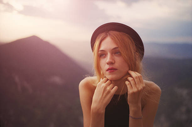Young woman in fedora hat on the mountains at sunset.