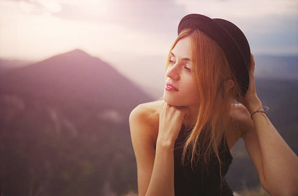 Young woman in fedora hat on the mountains at sunset.