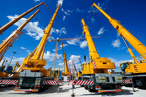 Mobile construction cranes Mobile construction cranes with yellow telescopic arms and big tower cranes in sunny day with white clouds and deep blue sky on background, heavy industry  construction machinery stock pictures, royalty-free photos & images